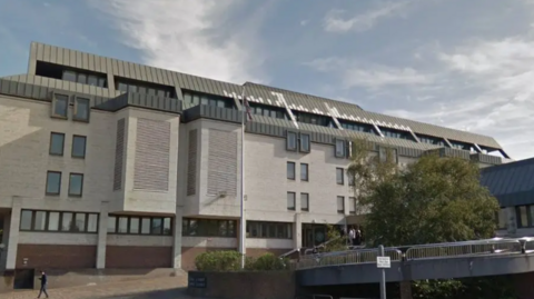 An exterior view of Maidstone Crown Court, a modern white building with black window fames and a grey slate roof.