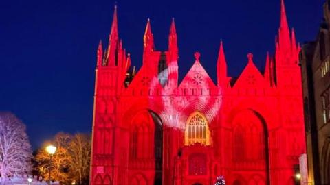 Peterborough Cathedral lit up in red light with a black sky in the background.