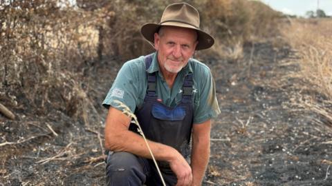 A man in a burned filed wears a cowboy style hat and looks at the camera with kind eyes.