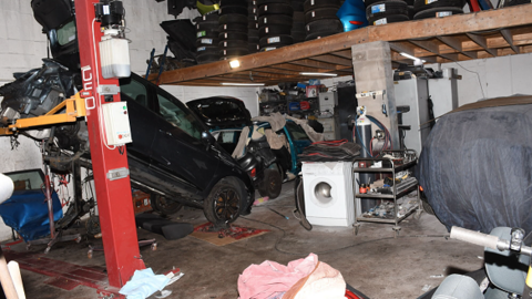 The inside of a garage showing a black cab suspended at its back end on a red metal column, while its front is resting on the ground