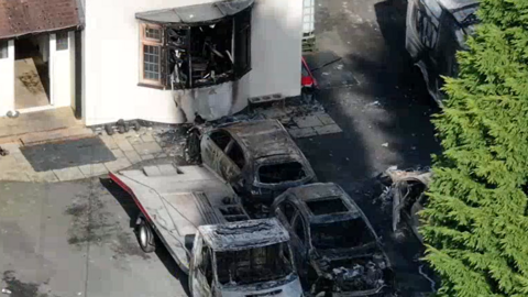 An aerial view of a house which had a burnt window and burnt vehicles out the front.