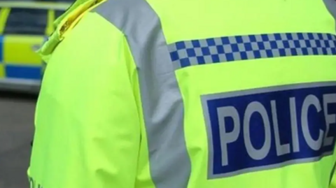 A close up of a police officer wearing a high visibility yellow jacket with police written on it.