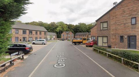 A Google street view image of Grey Fold. Several new build houses are situated either side of a road. A number of vehicles are parked outside.