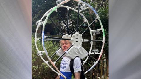 A man in running gear with a miniature big wheel resting on his shoulders