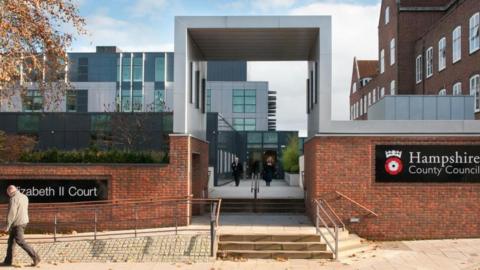 Hampshire County Council's HQ building. A stone archway leads into the building with a red brick facade. Steps lead down on to a pavement.