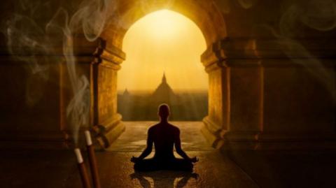 A person sits crossed legged looking out of a temple towards another