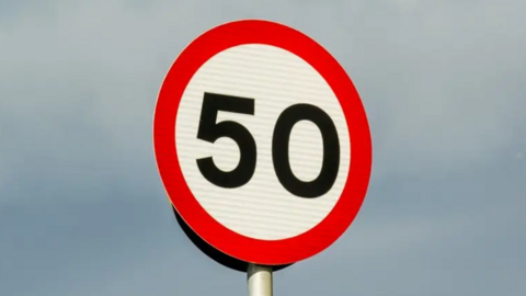 A 50 speed limit sign in black lettering surrounded by a red circle.
