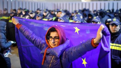 A Georgian opposition supporter holds an EU flag behind her in front of a row of police officers, during a protest in front of the office of the Georgian Dream ruling party in Tbilisi, Georgia, 28 November 2024