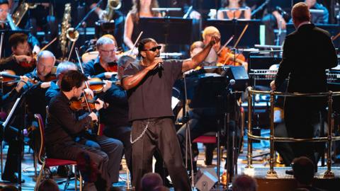 Luke James, dressed all in black, singing in front of the BBC Concert Orchestra in the Royal Albert Hall for the Proms