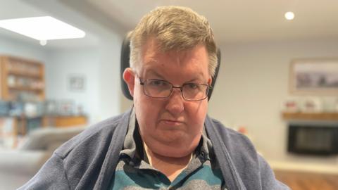 Middle aged man in glasses with a striped shirt and blue cardigan