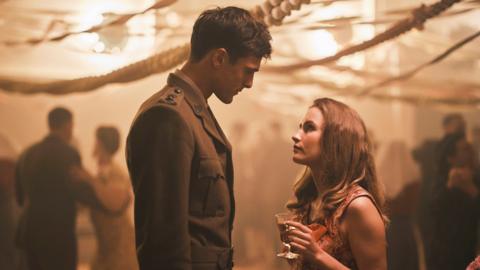 Two people at a party facing each other - one is in military uniform and one is in a dress.