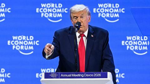 Donald Trump delivers a speech from a lectern at the World Economic Forum in Davos wearing a navy suit, red tie and a US flag pinned to his suit.