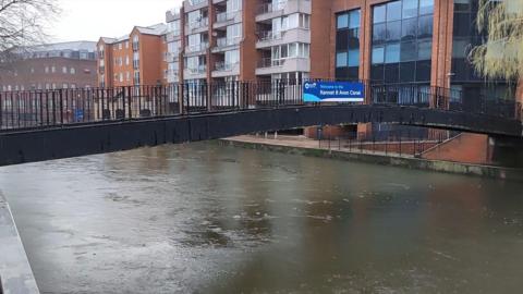 A view of the Orbit Footbridge in Reading. A sign on it reads "Welcome to Kennet and Avon Canal". It is an overcast day.