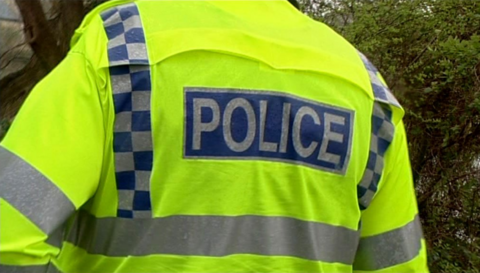 A photo of the back of a policeman in a yellow jacket