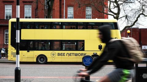 Yellow double-decker on Oxford Road with cyclist in hooded top and rucksack riding in opposite direction