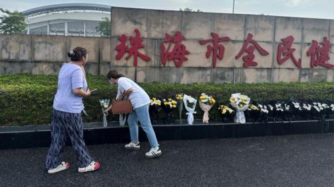 Two women place flowers outside the stadium in Zhuhai after the attack