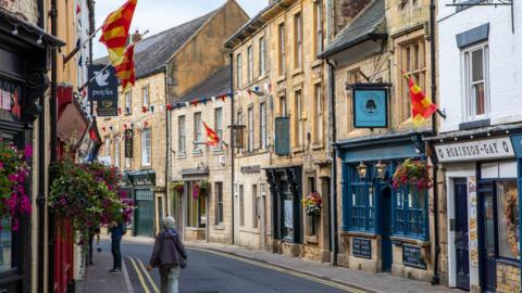 Hexham, a pretty market town with shop signs and flags hanging above the pavement. A woman can be seen walking away.