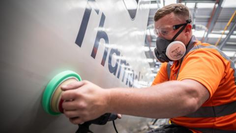 A man in orange hi-viz cleans the outside of a white Thameslink train.
