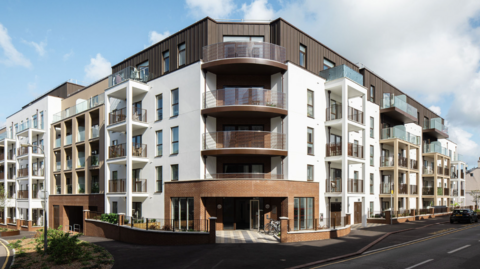 A busy coastal harbour with many small boats lined up along the shore and large crowds gathered by the water on a sunny day.
