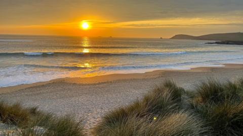 vivid yellow sun setting over the sea with beach and dunes in foreground 