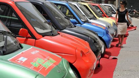 An Indian woman walks past a line of electric Reva motorcars prior to a Reva car rally held to celebrate World Environment Day in New Delhi on June 5, 2009.