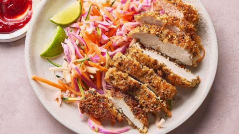 A plate with crispy fried chicken sliced up, next to coleslaw and lime wedges.
