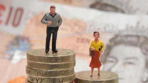 Plastic models of a man and woman stand on a pile of coins and bank notes