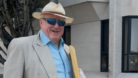 Gwynoro Jones outside Swansea Crown Court. He's wearing a hat, sun glasses, beige suit and open collar blue shirt