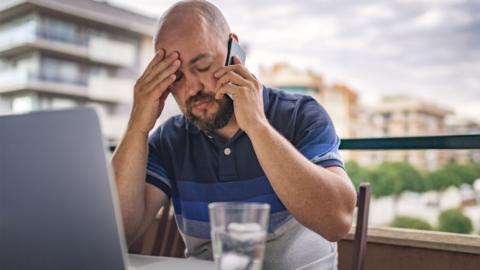 A man on the phone and his laptopwithis his palm to his forehead