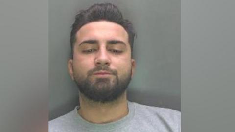A mugshot of Razvan wearing a grey sweater and looking down rather than at the camera. He has dark brown hair in a smart hipster style, and a beard and moustache.