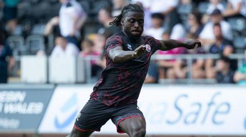 Kabongo Tshimanga running with one arm out and the ball at his feet during a pre-season match for Crawley in August 2025