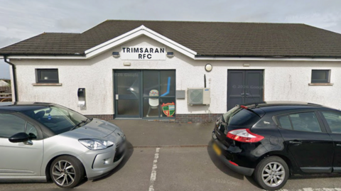 A white building with two cars parked in front of it. On the building it reads: Trimsaran RFC.