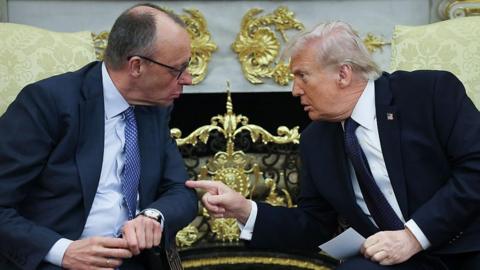 Trump and Merz speak in the Oval Office. They are seated and lean towards each other. Trump points a finger at Merz