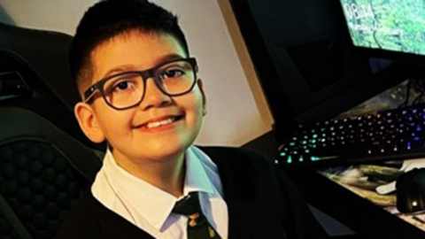 Twelve-year-old Azaad Khan in his school uniform sitting next to a computer 