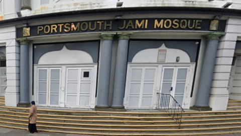 A sign in gold above a white building with grey pillars, wide steps and French windows reads "Portsmouth Jami Mosque"