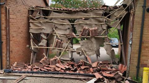 Wooden debris and roof tiles are scattered on the floor and hanging from the remains of an entranceway