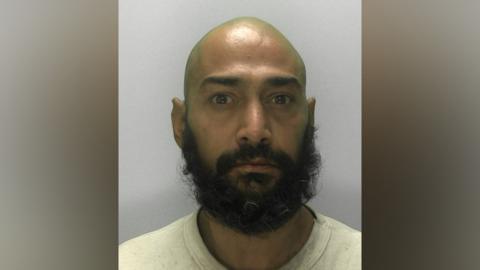 Afzul Veshima, a man with a bald head and bushy black beard, stares straight ahead in police photo