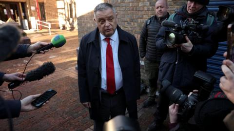 MP Mike Amesbury outside court, surrounded by reporters with cameras and microphones.