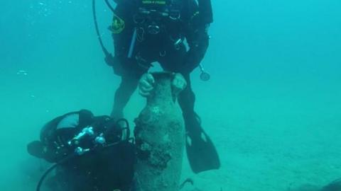 A diver holds an ancient clay jar under the sea after excacvating a ship wreck