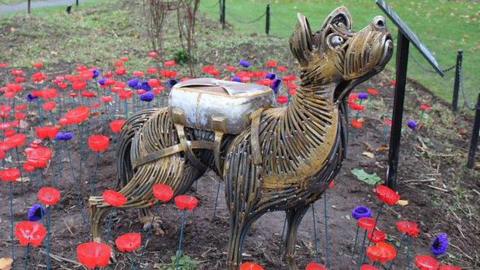 Metal sculpture of Bing seen standing in a flower bed surrounded by red and purple poppies 