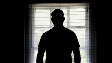 The silhouette of a man from the back looking out of a bay window with a slatted blind