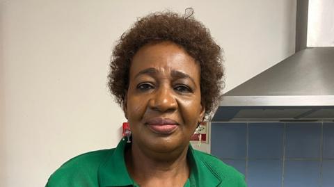 Maria Affa in the kitchen at Fishermead Trinity Centre. She is wearing a green blouse and a green apron.