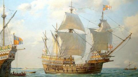 An artist's painting of the Mary Rose. It is a large, wooden ship with huge white sales and a St George's flaf flying at the front. The bow of another ship can be seen to the left of the Mary Rose. 