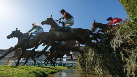 Horses jump over a fence at the Grand National