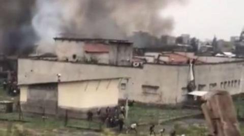 Black smoke billows from the prison's building as people flee from inside