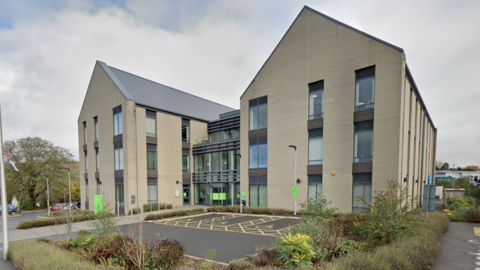 A Google street view picture of the front of East Devon District council's building. It is a cream coloured building with a car park at the front.