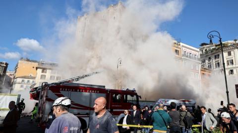 A plume of dust is visible with a fire truck and rescue workers standing in front