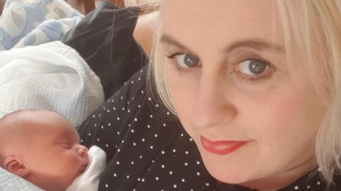 A woman with blonde hair holds a newborn baby