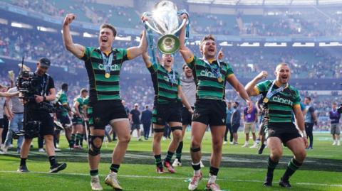 Northampton players walk around the field holding the Premiership trophy