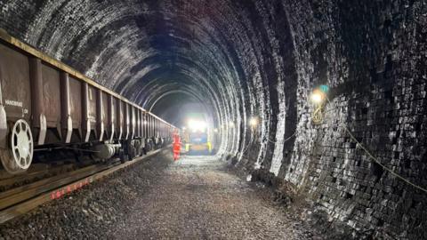Track renewal work taking place inside a tunnel with a man in orange high viz near machinery